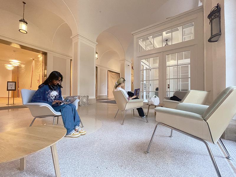 two women sit with laptops on modern chairs in restored lobby 